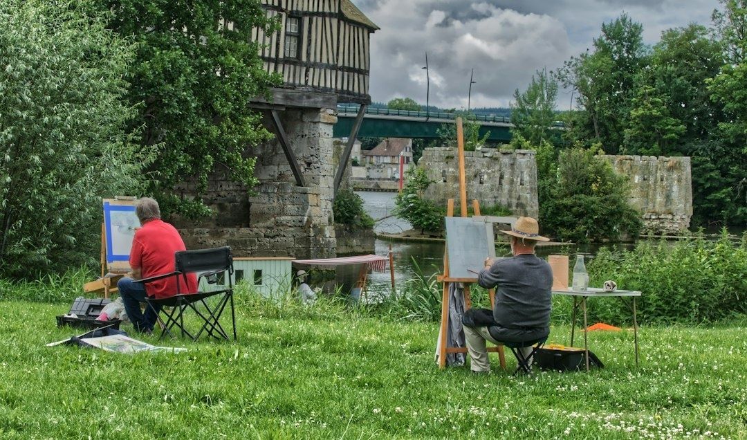 Two plein-air painters work beside a river and historic stone ruins