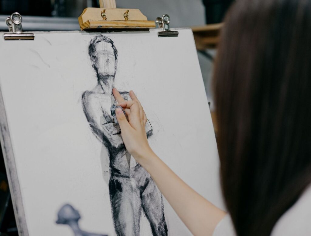 Artist adding charcoal shading to a figure drawing on an easel